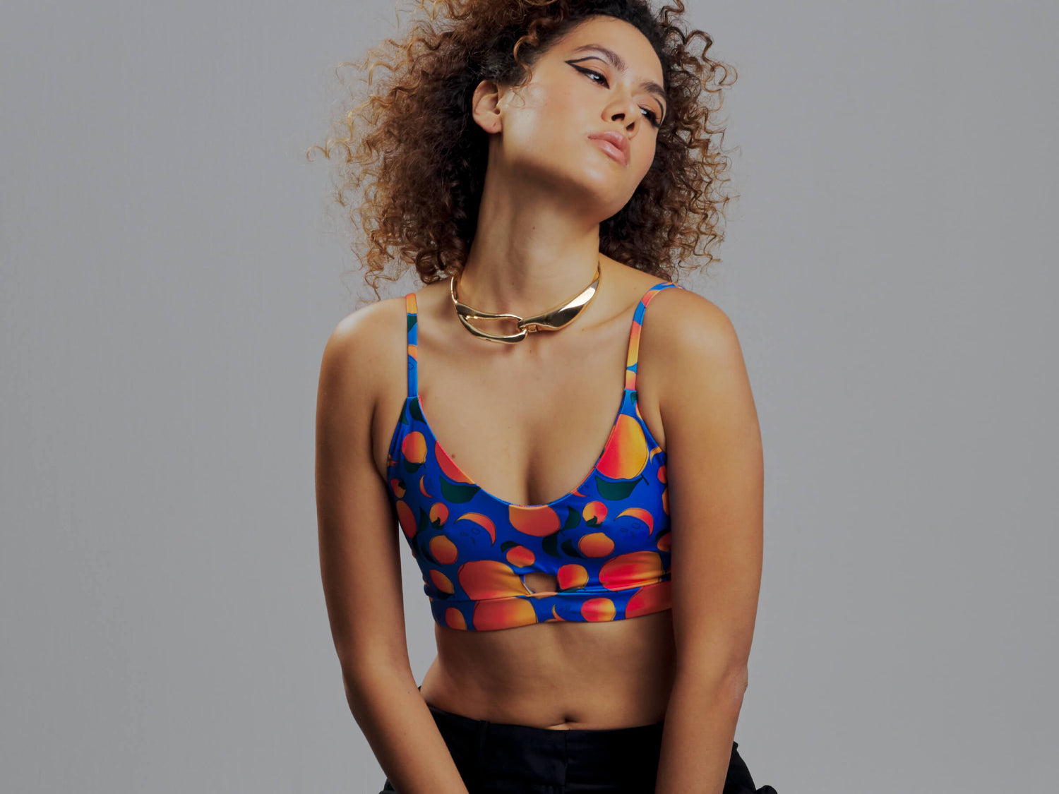 woman wearing a terracotta brown sports bra with palm trees and flowers and a black and white striped band. She has a black blazer and silver necklace with her hair up.