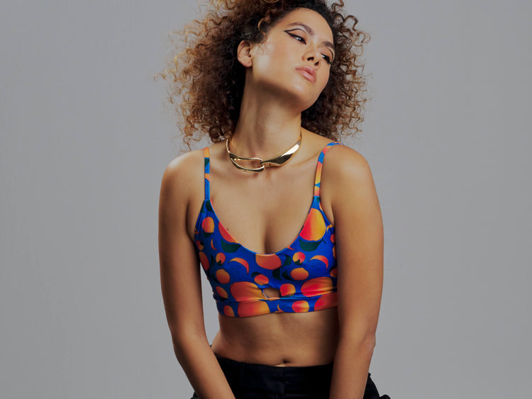 woman wearing a terracotta brown sports bra with palm trees and flowers and a black and white striped band. She has a black blazer and silver necklace with her hair up.